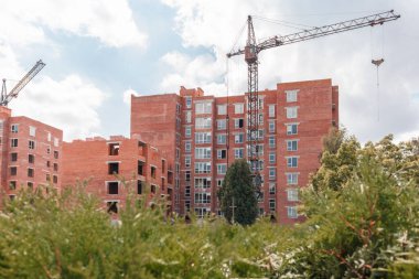 Çok katlı yeni binaların inşaatı. Yeşil çalıların arkasındaki inşaat alanında.