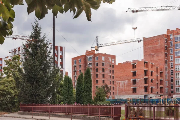 İnşaat alanı ağaçlarla döşenmiş. Çok katlı yeni binaların inşaatı. İnşaat vinci evlerin yanında.