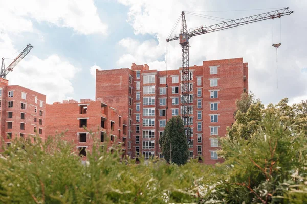 Çok katlı yeni binaların inşaatı. Yeşil çalıların arkasındaki inşaat alanında.