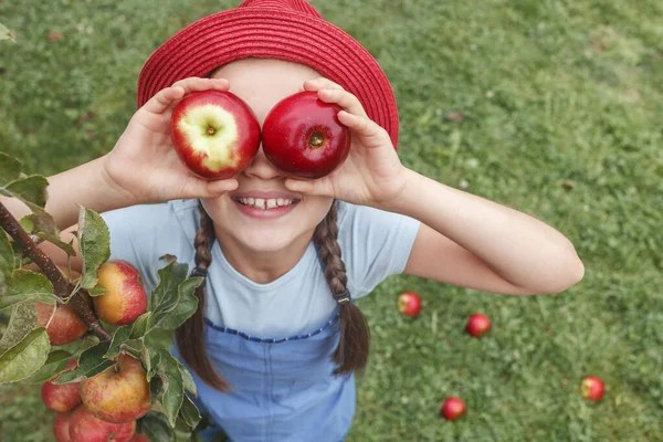 Niña Con Sombrero Rojo Sostiene Dos Manzanas Cerca Los Ojos — Foto de Stock