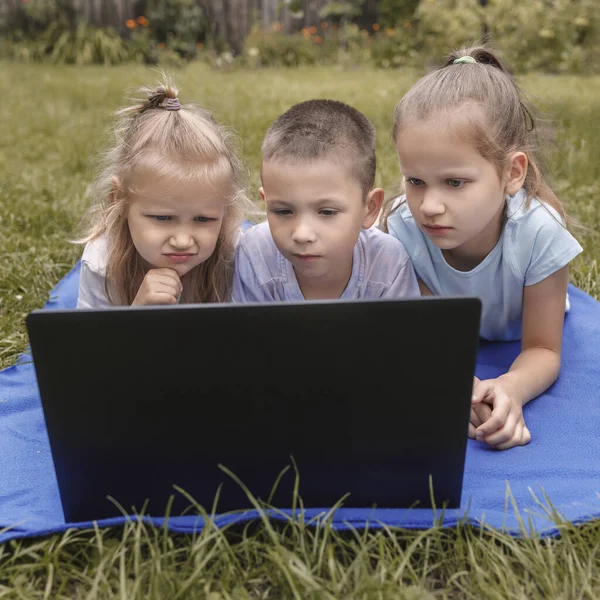 Tre Barn Studerar Noggrant Bärbar Dator Som Ligger Marken Trädgården — Stockfoto