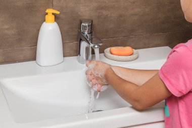 Küçük kız ellerini banyoda sabunla yıkıyor. Enfeksiyon ve virüslere karşı koruma.