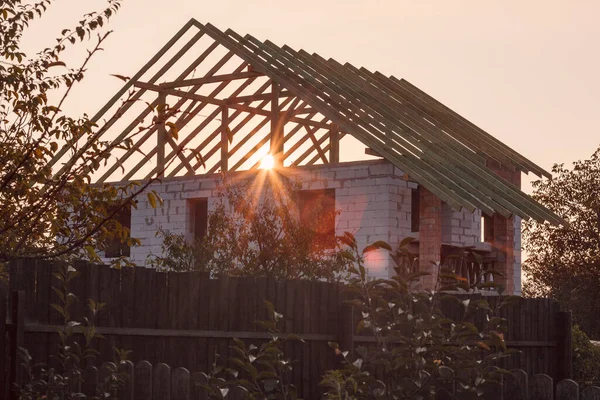 The sun shines through the roof structure of the house. Construction of a new house at sunrise. Dream of your own home