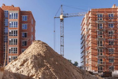 Çok katlı bir binanın yanındaki vinç iskelesi ile döşenmiş. Tuğla evlerin arka planındaki inşaat sahasına kum yığını