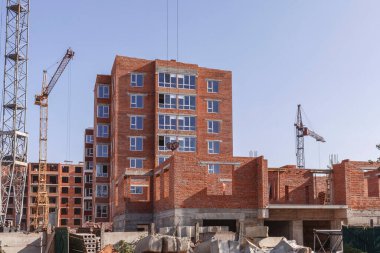 Çok katlı bir binanın yakınındaki kule vinçleri. Beton blokları ve zemin panelleri olan inşaat alanı