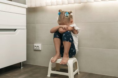 Banyoda ağlayan küçük bir kız. Kız küçük bir sandalyede oturuyor ve elleriyle yüzünü örtüyor.