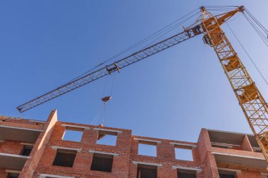 Kule vinci çok katlı bir binanın yakınında çalışıyor. Mavi gökyüzünün arka planında kule vinci