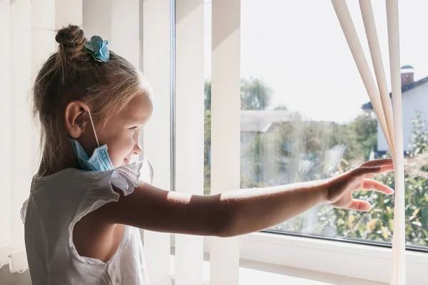 Little Girl Medical Mask Looks Out Window Throwing Away Blinds — Stock Photo, Image