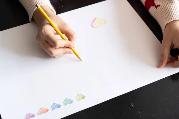 girl draws a pencil heart on paper. DIY card for valentines day. view from above