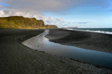 Vik, Güney İzlanda küçük dere yansıması ile siyah kum plaj.