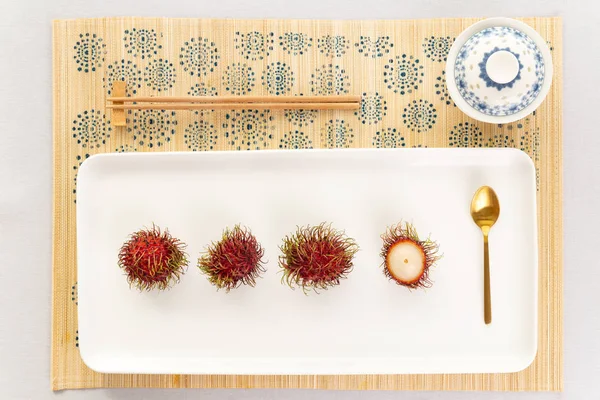 Elegant rambutan asian desert top view with traditional chinaware bowl for tea, golden spoon and chopstick in a white and pure ambiance.