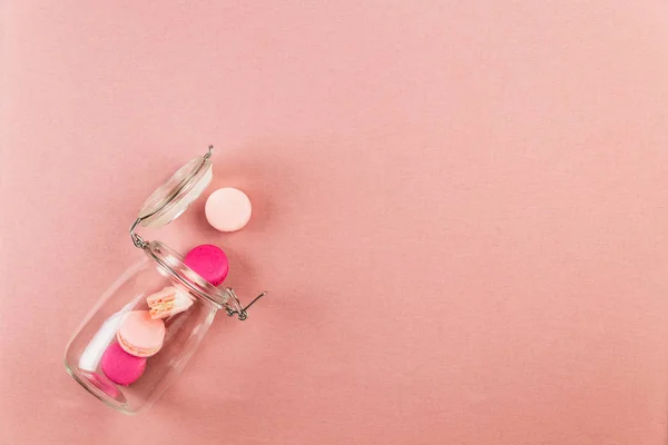 Macarons ou macarons roses et magenta français, tombant d'un bocal en verre sur un fond de nappe rose avec espace de copie . — Photo