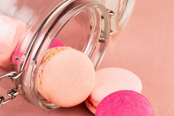 Růžová Francouzská makaróny nebo makaroony, které padají ze skleněné sklenice na růžovou tkaninu, šatna. — Stock fotografie