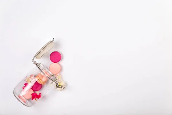 프렌치 핑크 마카롱 또는 마카롱, 체리 꽃, 분홍색 화신 꽃잎이 카피스페이스가 있는 흰색 배경에 유리 항아리에서 떨어지는. — 스톡 사진