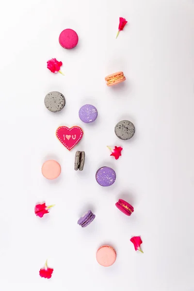 Pink, magenta, grey and purple French macarons or macaroons, with I love you cookie and pink incarnation petals spread on a white background in top view. — Stock Photo, Image