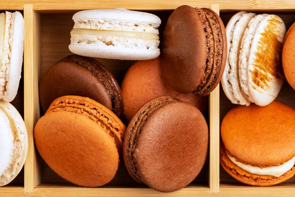 Brown and white french macarons or macaroons, (chocolate, coffee, toffee, salted caramel and vanilla) stacked in a three compartments bamboo box. — Stock Photo, Image