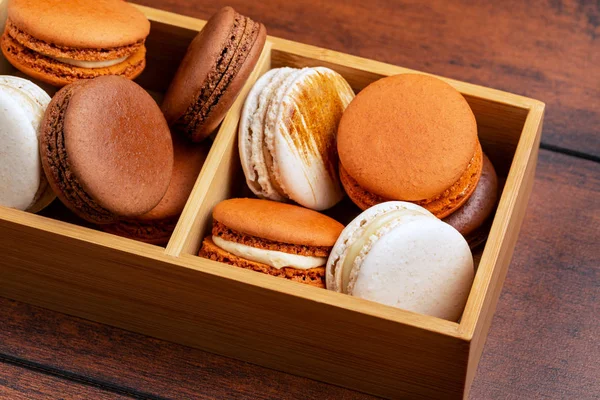 Brown and white french macarons or macaroons, (chocolate, coffee, salted caramel and vanilla) stacked in a compartment bamboo box. Side view. — Stock Photo, Image