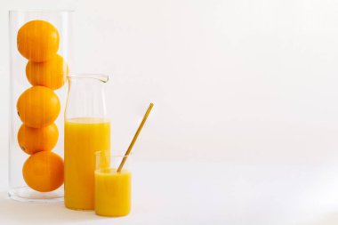 Beyaz bir arka plan üzerinde portakal dolu uzun bir cam tüp tarafından bir bardak ve bir sürahi portakal suyu.