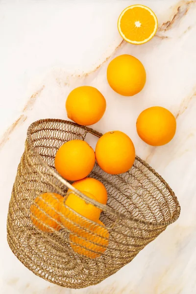 Oranges spreading out of a golden basket over a marble background. — Stock Photo, Image