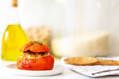 Akdeniz domatesleri et, ekmek kırıntıları, biberiye, kekik, maydanoz ve zeytinyağı küçük beyaz bir tabakta mutfak havlusu, zeytin ağacı servis kaşığı, zeytinyağı şişesi ve mermer üzerinde kahverengi ve beyaz pirinç kavanozları.