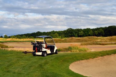 Golf arabası kumlu zeminin yanındaki golf sahasında, yeşil zemin ve arka planda orman. Golf sporu 