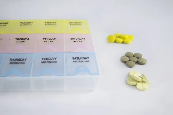 Yellow, gray, and white round pills near pill box. Pill container on a gray background. Medical organizer. Weekly treatment plan. Pill case close up.  Patient self-care.