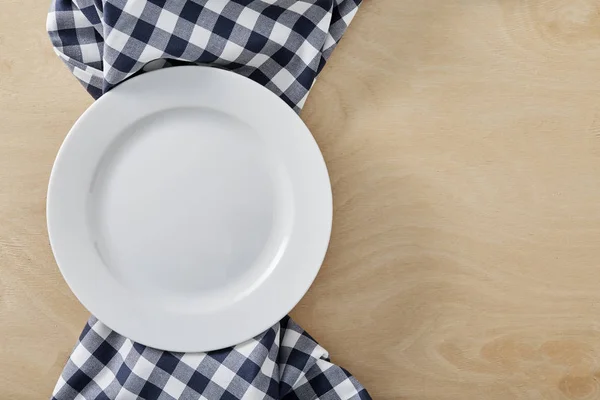 Textile blue cell napkin on wooden table with copy space and white empty plate — Stock Photo, Image