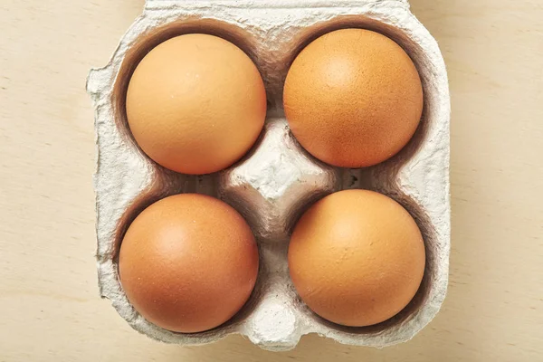 Quatre œufs crus dans l'emballage sur une table en bois . — Photo