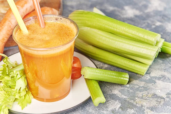 Fresh green celery, juice in glass on background near the carrots.