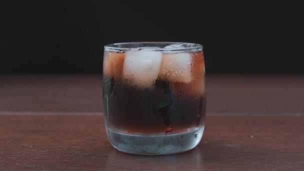 Stukje ijs valt in glas cola. — Stockvideo