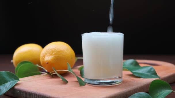 Gießt Zitronensaft aus Krug in Glas auf Holztisch. — Stockvideo