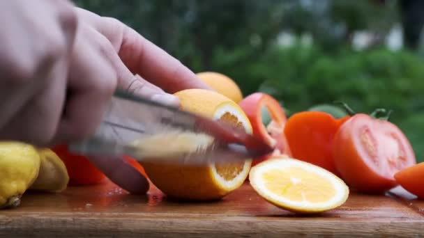 Hand schneidet Orange mit einem Messer auf Holzbrett. — Stockvideo