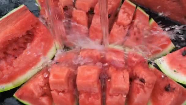 Wasser mit Spritzern über rote Wassermelone auf schwarzem Hintergrund gießen. — Stockvideo