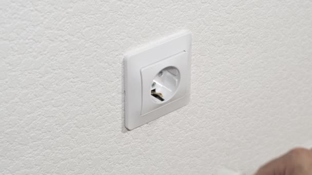 Hand puts a white power plug in the wall socket — Stock Video