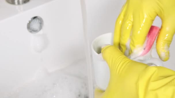 Person in gelben Gummihandschuhen wäscht einen Becher in der Spüle — Stockvideo
