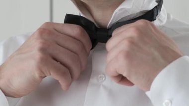 Beyaz gömlekli adam siyah bir kelebek giyiyor.