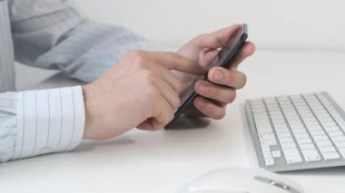 Elinde akıllı telefon tutan ve çalışma masasına mesaj yazan bir adam..