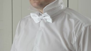 Beyaz gömlekli adam kelebek takıyor.