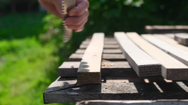 Close-up shot van een hand snijden door een houten plaat. Een man gebruikt een handzaag — Stockvideo