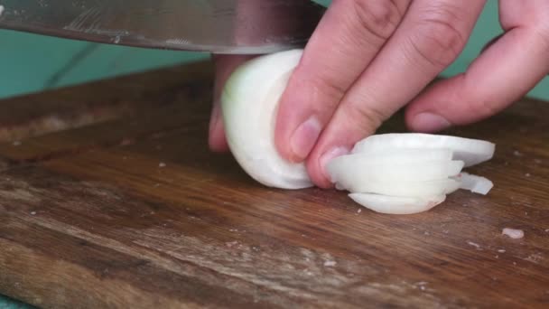 Разрезание белого лука на ломтики ножом на деревянной доске — стоковое видео