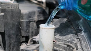 Adam özel temizlik malzemeleri şişesini araba temizleme tankına boşaltıyor.