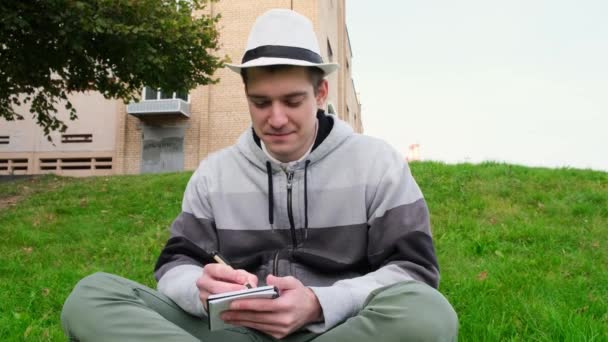 Genç bir adam halka açık bir yerde oturur ve kağıda kalem notları yazar. Kapat. — Stok video