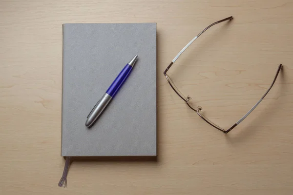 Gray diary, blue pen and glasses on a brown table top view. Office desk table concept — Stock Photo, Image