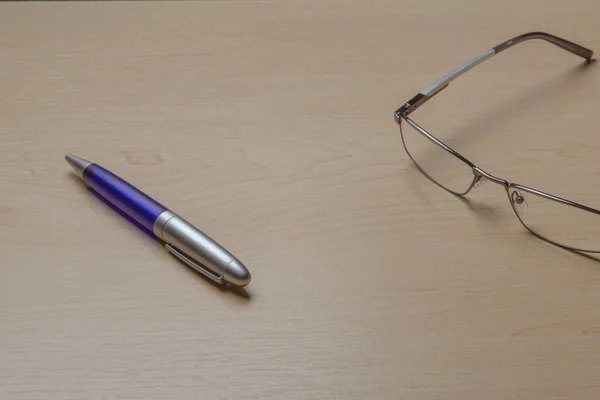 Blue pen and glasses on the office brown desk, selective focus — Stock Photo, Image