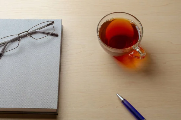 Gray diary, cup of tea, blue pen and glasses on a brown table, selective focus — Stock Photo, Image