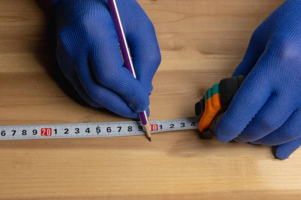 Carpintero en guantes azules con un lápiz marca el espacio en blanco para muebles de madera —  Fotos de Stock