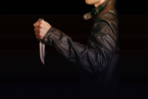Человек в черной кожаной куртке с ножом в руке на черном фоне — стоковое фото