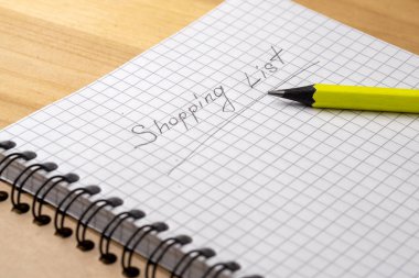 Ahşap bir masada bir kafeste çarşaf ile bir defter üzerinde sarı kalem. Alışveriş listesini imzala