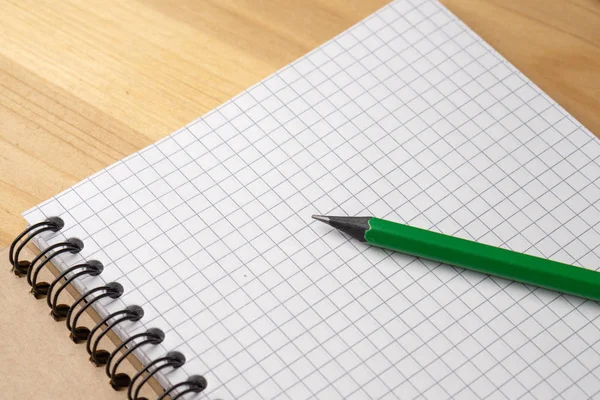 Green pencil on a notebook with sheets in a cage on a wooden table — Stock Photo, Image