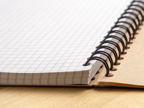 Notebook with checkered sheets on a wooden table. Side view — Stock Photo, Image